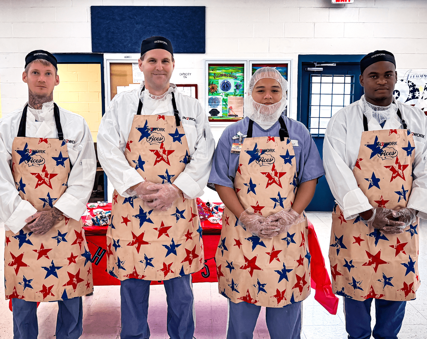 A group of people stand behind together in front of a table with aprons on. 